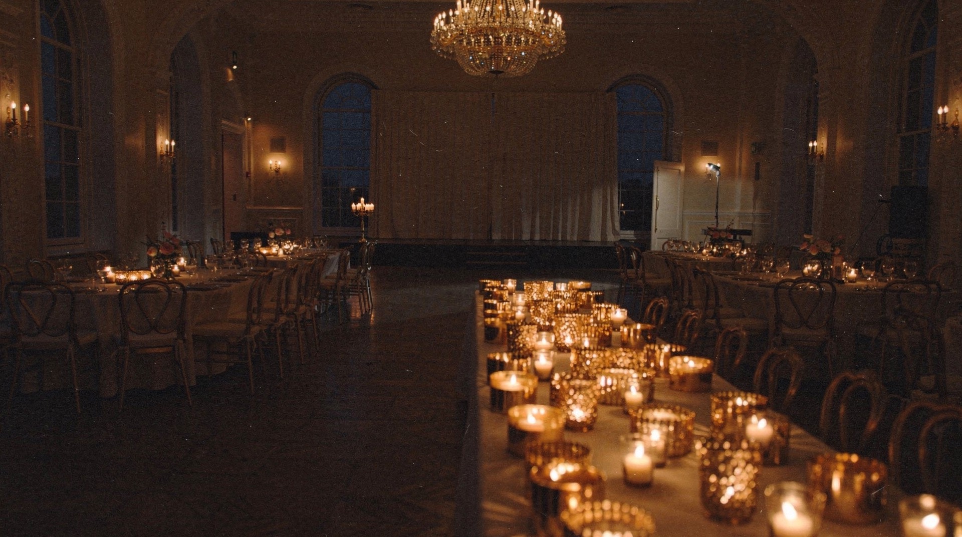 Derselbe Festsaal bei Nacht: lange Tafel voller Kerzen in goldenen Gläsern, Kronleuchter